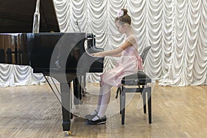 Girl in a beautiful pink dress playing on a black grand piano. Girl playing on a black piano.