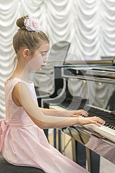 Girl in a beautiful pink dress playing on a black grand piano. Girl playing on a black piano. Vertical photo photo