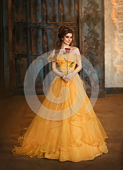 Girl beauty fantasy princess in yellow long historical, medieval silk dress holding flower red rose in her hands