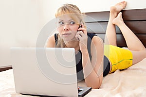 Girl on bed with laptop and calls at phone