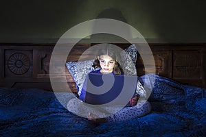 Girl in bed with laptop, glowing light.