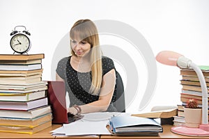 Girl behind the desk littered with books smiling in a laptop information gathering