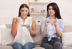 Girl being envious her friend`s victory in mobile game indoor