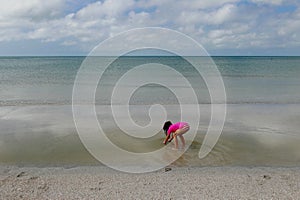 Girl bending over in shallow water in calm ocean water