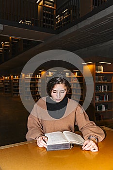 Girl bent over book sitting in library alone