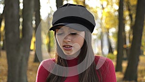 Girl in a beret rejoices, poses and looks flirty at camera in sunny autumn park