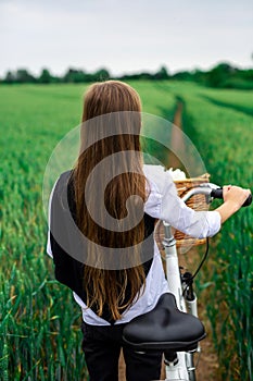 A girl on a bicycle with a basket in the middle of a wheat field