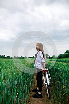 A girl on a bicycle with a basket in the middle of a wheat field