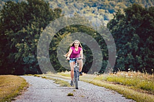 Girl on bicycle cycling down a dirt path in summer