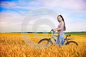 Girl with a bicycle on the wheat field