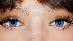 A girl with big blue eyes looks at the camera close-up. Macro shot of blue eyes. The girl is made using computer