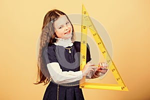 Girl with big ruler. School student study geometry. Sizing and measuring. Kid school uniform hold ruler. School photo