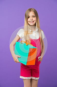 Girl with big smile holding colorful paper bag. Model with orange and green gift box. Child with long blond hair wearing