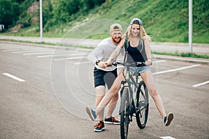 Girl on bike, guy runs. boy teaches girl to ride a bike. Morning Meadow.