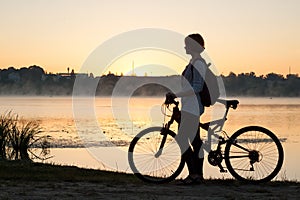 A girl with a bike near the lake in the summer morning