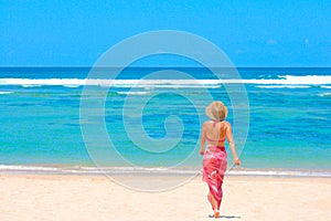 Girl in bikini and pareo walking towards ocean