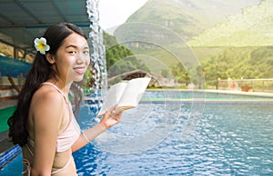Girl in bikini reading a book by the pool