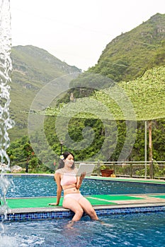 Girl in bikini reading a book by the pool