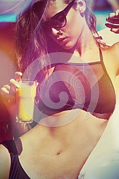 Girl in bikini and sunglasses by the pool with juice