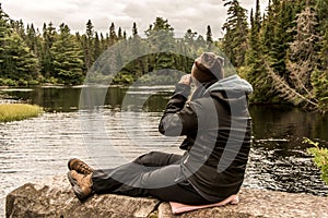 Girl with binocular sitting near Lake of two rivers in Algonquin National Park Canada Ontario natural pinetree landscape