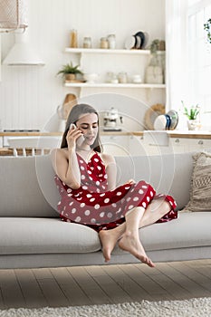 Girl blab on smartphone seated on sofa at home