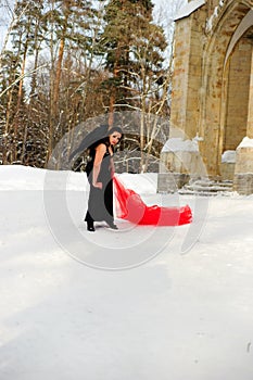 Girl with black angel wings in a black dress in winter and red flowing fabric