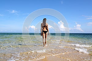 Girl in black bikini walking on the white beach