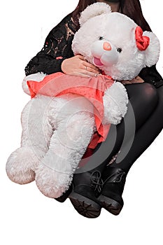 A girl in black clothes in a sitting position holds a large soft white toy of a fluffy bear girl on an isolated background