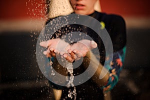 Girl in the black diving suit standing under the shower place hands under water