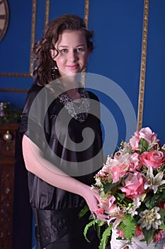 Girl in a black dress next to a vase with flowers