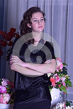 Girl in a black dress next to a vase with flowers