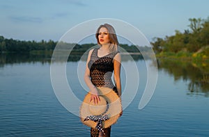 Girl in a black dress by the river in the last rays of the sun