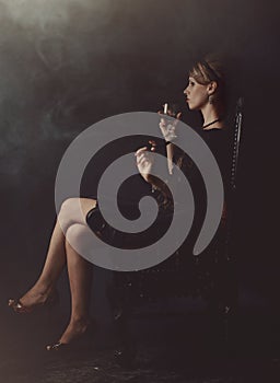 A girl in a black dress is sitting on a chair with a glass of wine