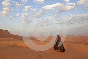 Girl in black dress walking in desert of Sharjah, United Arab Emirates.. back view