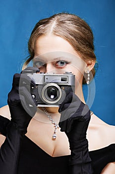 The girl in a black evening dress and long gloves is holding a film long-range camera in her hands