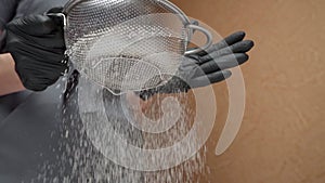 A girl in black gloves and a gray apron sifts through flour, close-up