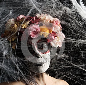 Girl with black hair is dressed in a wreath of multi-colored roses and makeup is made on her face Sugar skull to the day of the