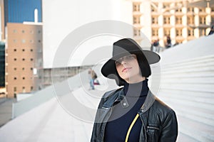 Girl in black hat and jacket pose on stairs