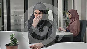 Girl in black hijab sits in the office and coughs, a disease, a cold, an illness is a concept. Girl in pink hijab in the