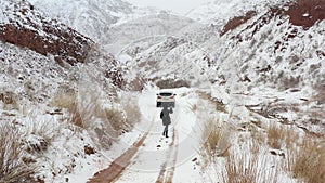 A girl in a black hooded jacket walks along a snowy mountain road to a white SUV