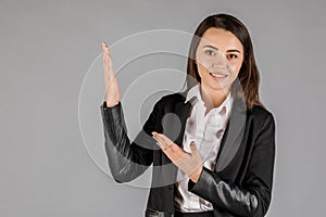 Girl in black jacket on grey background pointing up