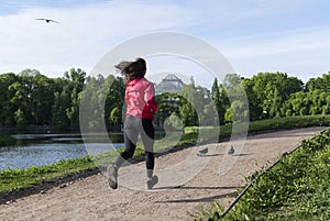 Girl in black leggings and a red jacket running down the path in the Park