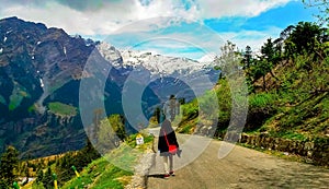 A girl in a black long coat and a red crossbody bag walking along the path to the Himalayan mountains.