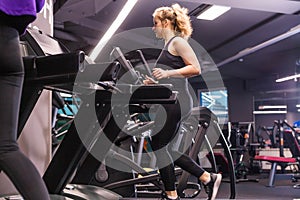 A girl in a black sports uniform runs on a treadmill in a sports hall