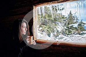 A girl with a black sweatshirt in a log cabin looks at a cup of hot tea. With a smile