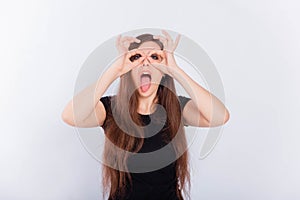 Girl in a black T-shirt with long hair grimaces and shows glasses with her hands isolated on a white background.