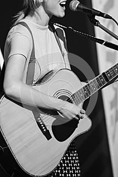 Girl black and white with a guitar sings near the microphon