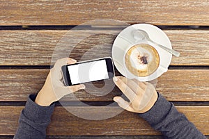 Girl with a blank cell phone and a cup of coffee at a wooden tab