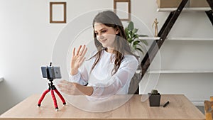 Girl blogger recording video blog for social network sitting at her desk at home. A woman vlogger waves her hand at the