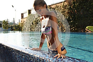 Girl with blond hair in elegant bikini relaxing in swimming pool